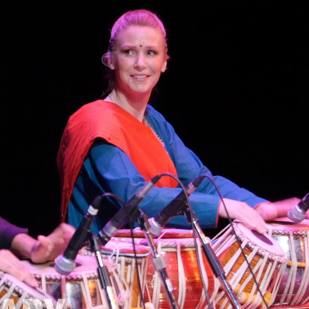 Melissa playing tabla on stage under blue and orange stage light.