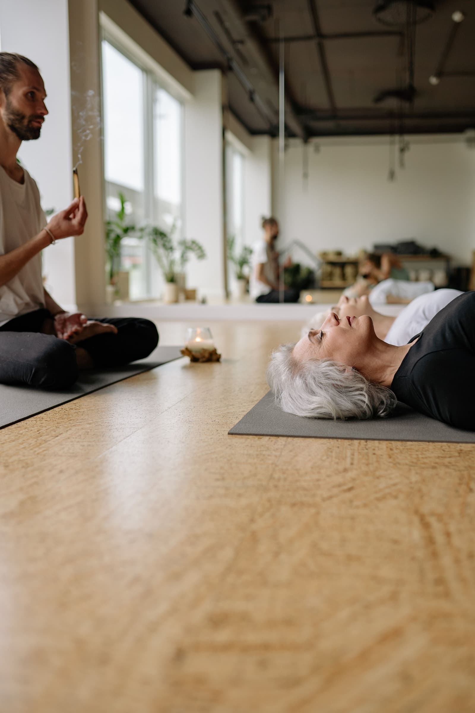 An older woman resting on a mat while an instructor sits nearby.